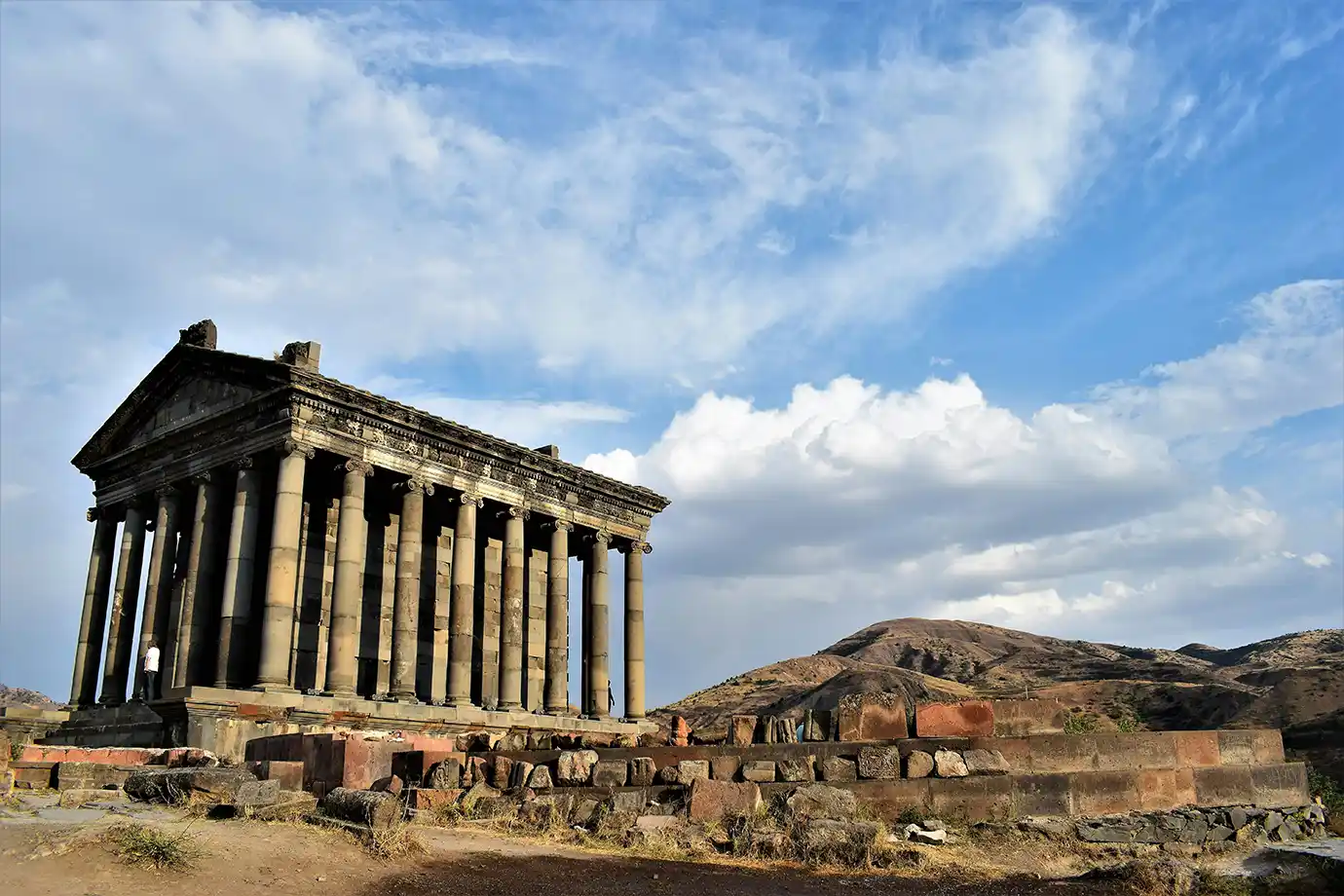 The stone Ionic columns and triangular pediment of Garni Temple under a blue sky with soft white clouds featured in a travel guide on The Ultimate 7-Day Armenia Itinerary.