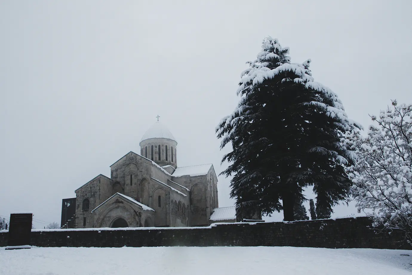 A serene winter landscape showing Gelati Monastery surrounded by snow-covered ground and evergreen trees, highlighting historical Places to Visit in Georgia.