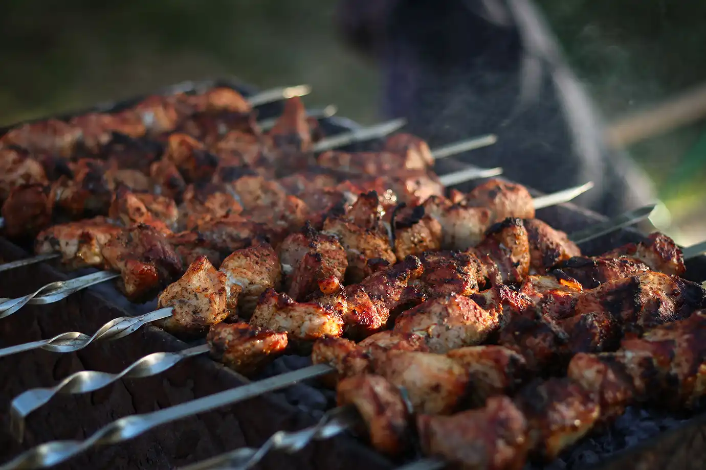 Marinated pork chunks grilling over hot coals on metal skewers to make traditional Mtsvadi barbecue, highlighting essential dishes for a Georgian Food Guide.