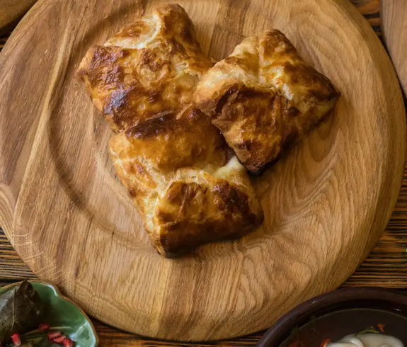 A flat lay spread of traditional dishes including penovani khachapuri, badrijani nigvzit, and dolma on wooden serving platters for a Georgian Food Guide.