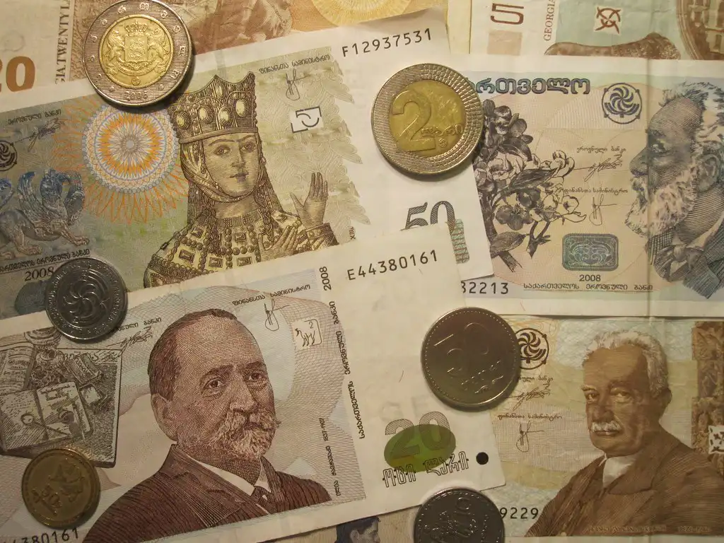 A close-up view of various Georgian Lari banknotes and coins scattered across a surface, representing currency budgeting for Georgia Travel Cost.