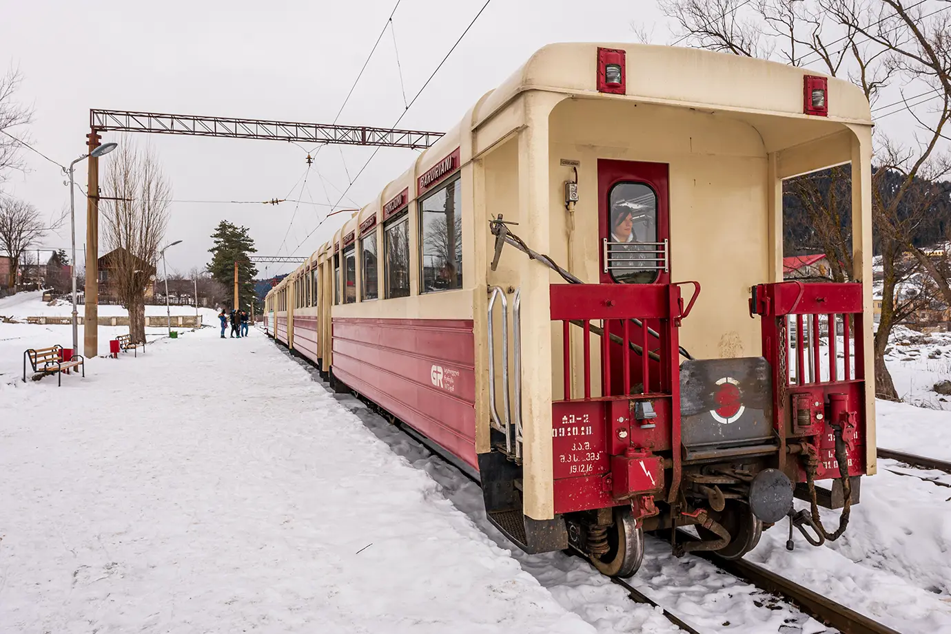 A red and cream vintage train sitting on snow-covered railway tracks at a winter station platform, highlighting affordable intercity transit for Georgia Travel Cost.