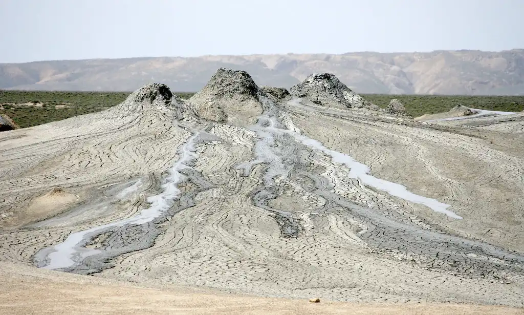 Bubbling grey mud volcano cones oozing wet mud across cracked earth in Gobustan featured in a travel guide on The Ultimate 7-Day Azerbaijan Itinerary.