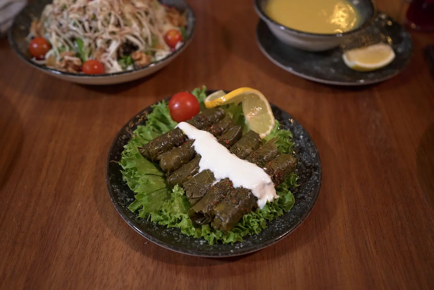 Stuffed grape leaf tolma drizzled with creamy garlic yogurt sauce on a bed of fresh lettuce featured in a culinary guide on What to Eat in Armenia.