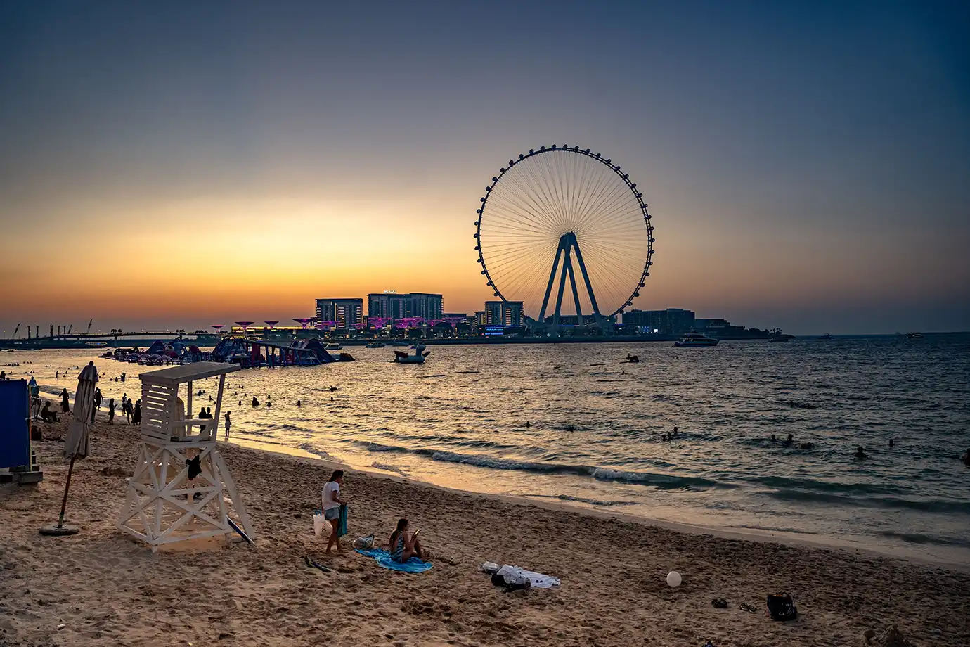 Visitors relaxing on the sandy shores of JBR Beach at sunset with Ain Dubai standing on the horizon, featured in Best Time to Visit Dubai.