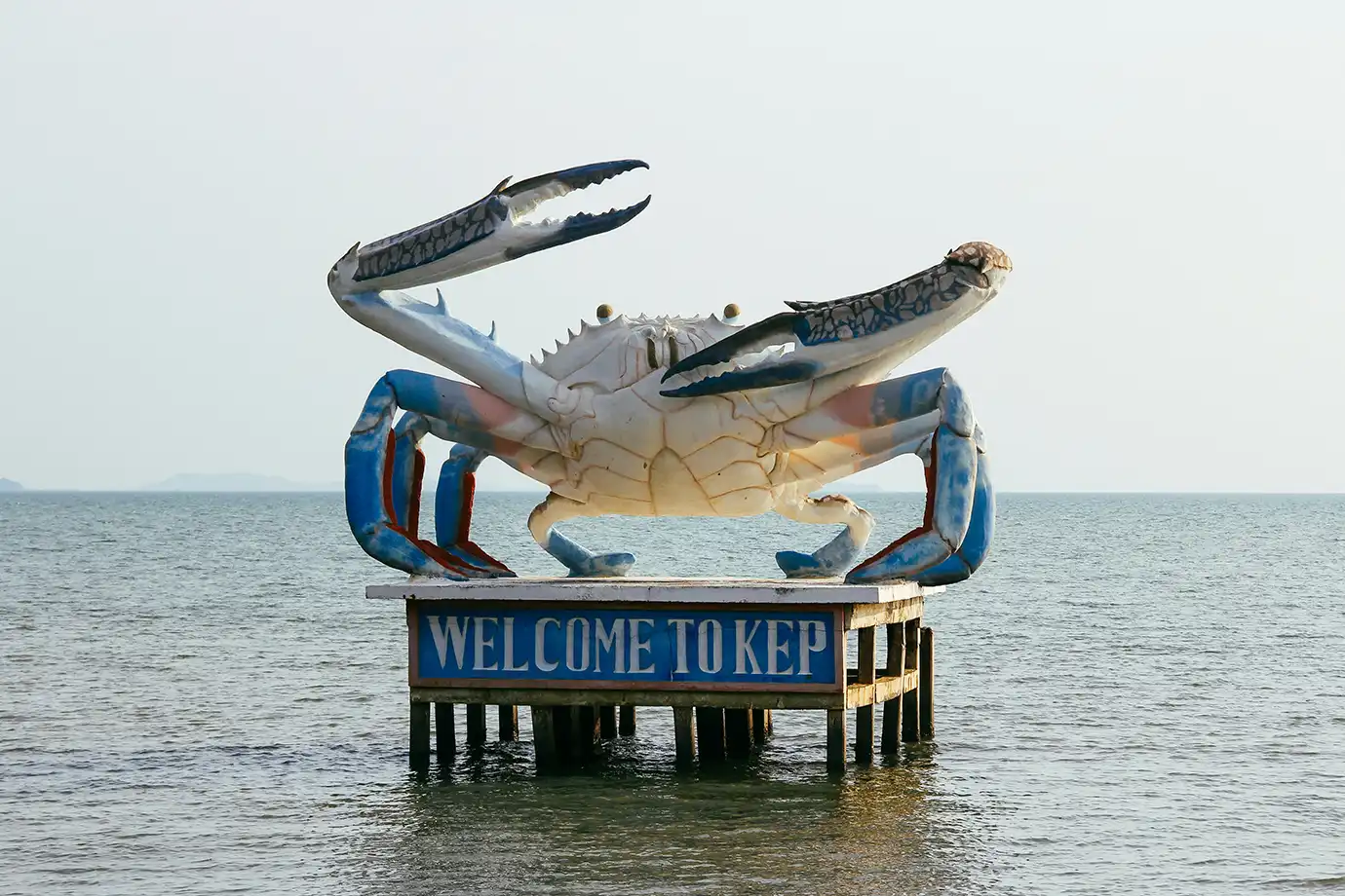 The large blue crab statue with "Welcome to Kep" sign mounted on stilts in the ocean featured in a travel guide on Cambodia Itinerary.