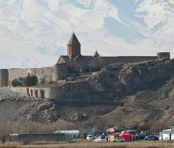 Historic Khor Virap Monastery complex perched on a rocky hill against a background of snow-covered mountains featured in a travel guide on 5 Must-See Monasteries in Armenia.