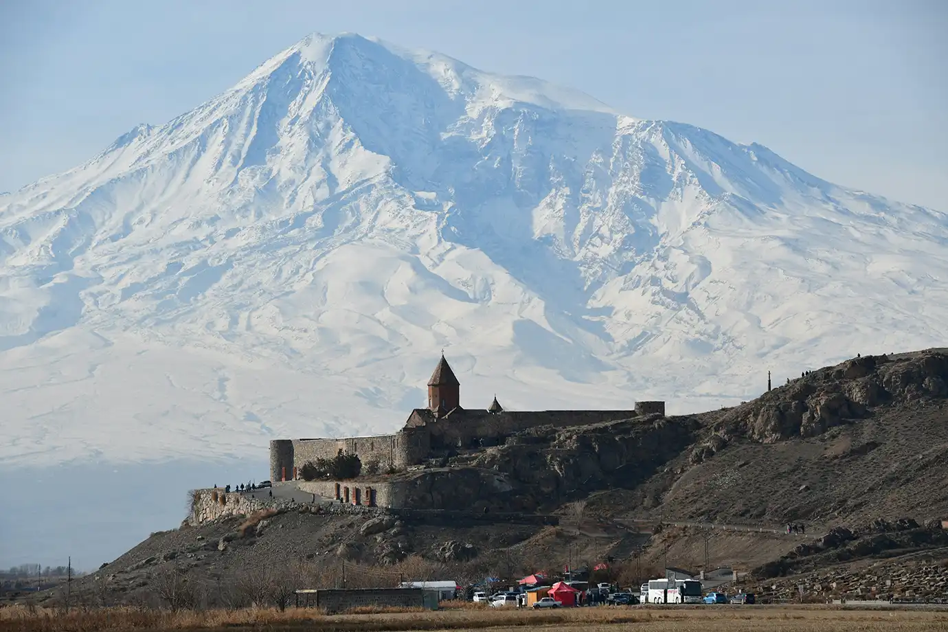 Ancient Khor Virap Monastery perched on a hill directly in front of the vast, snow-capped Mount Ararat featured in a travel guide on 5 Must-See Monasteries in Armenia.
