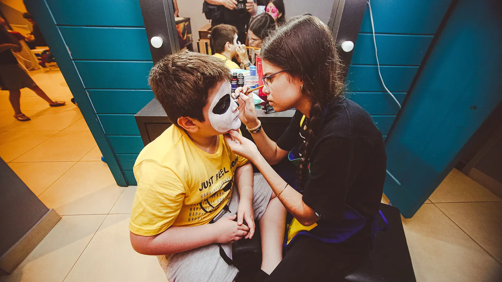 A young boy getting black and white skull face paint applied by an instructor inside KidZania, a popular indoor attraction when visiting Dubai with Kids.