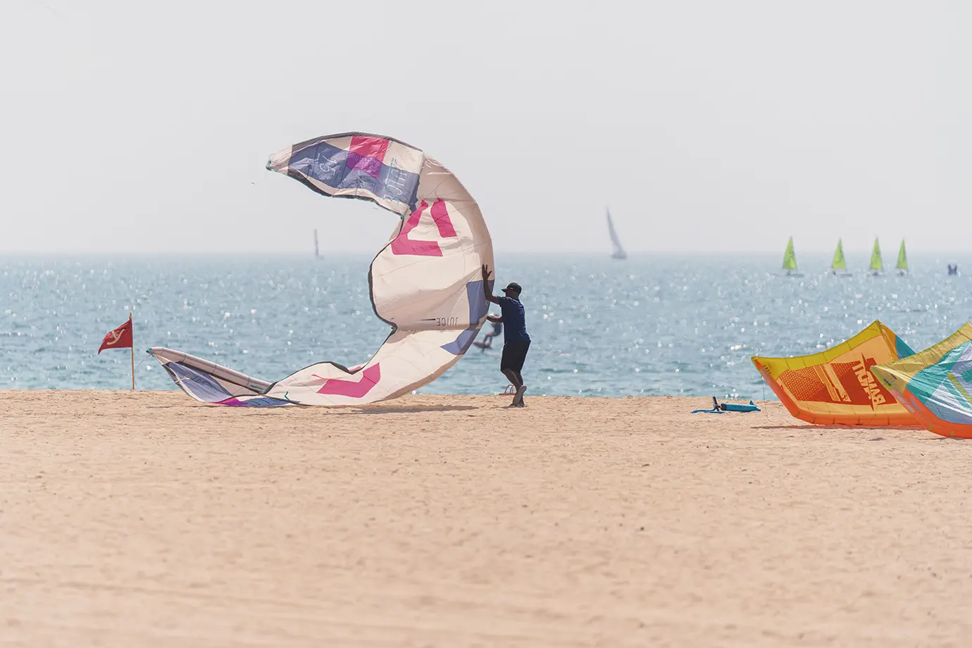 A person handling a colorful kitesurfing sail on the golden sand of Kite Beach, showcasing outdoor watersports and Things to Do in Dubai.