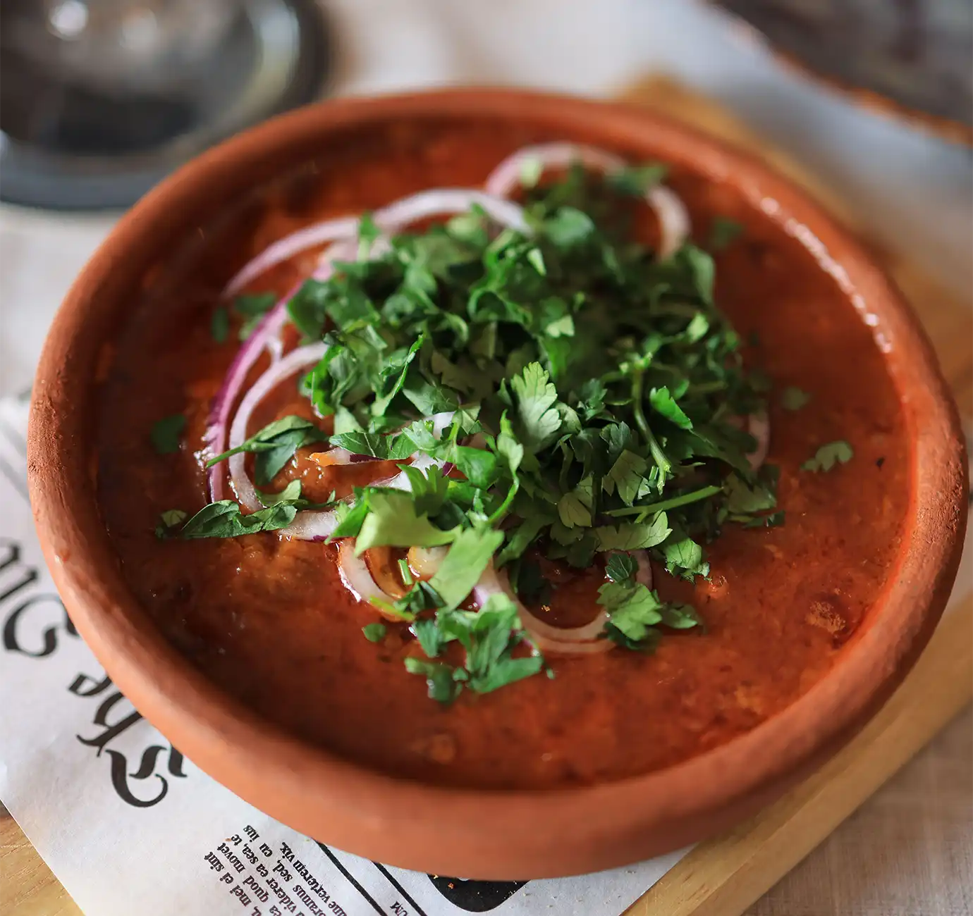 A clay pot filled with rich Lobio kidney bean stew topped with sliced red onions and fresh herbs, showcasing essential dishes for a Georgian Food Guide.