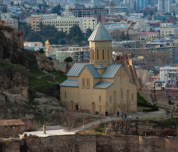 A panoramic view of Narikala Fortress and St Nicholas Church nestled along a rocky cliff overlooking Old Tbilisi, highlighting iconic Places to Visit in Georgia.