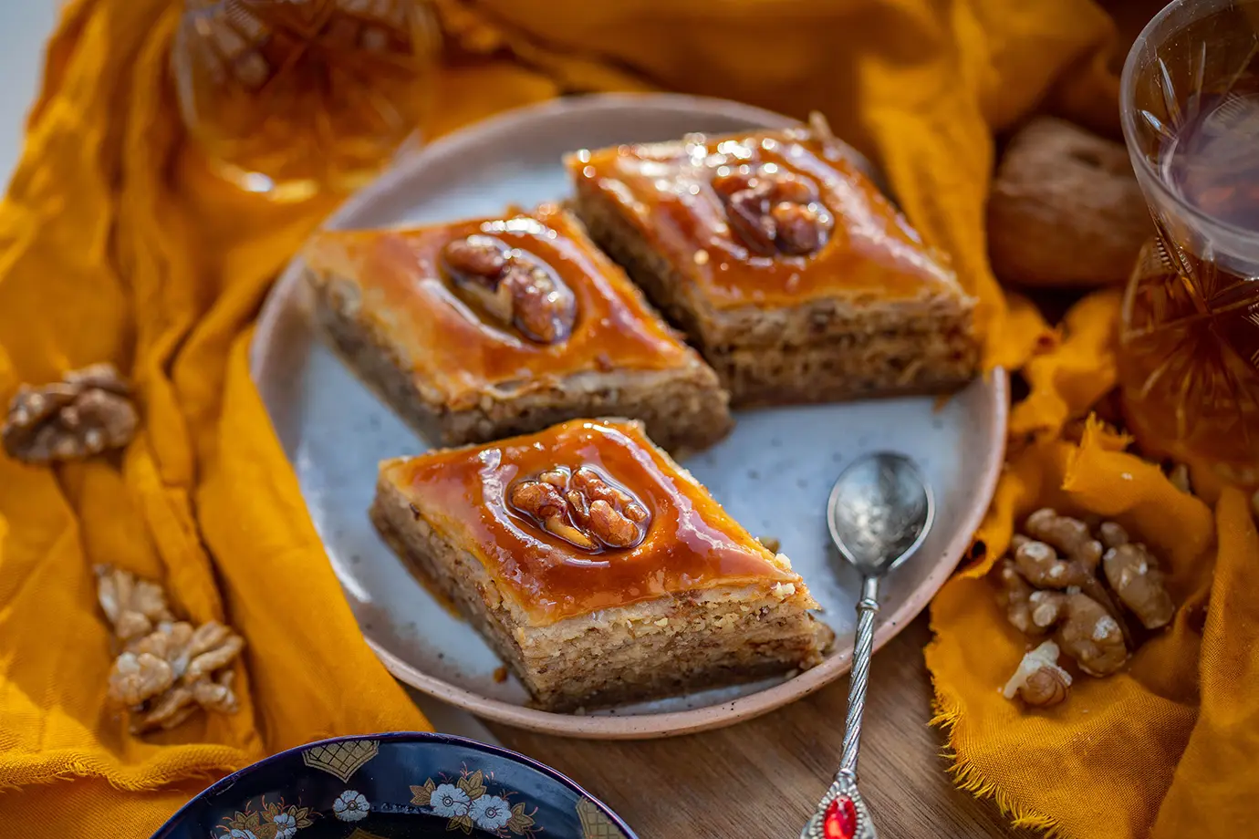 Diamond-cut golden Azerbaijani pakhlava pastries garnished with walnuts on a plate with tea featured in a travel guide on What to Eat in Azerbaijan.