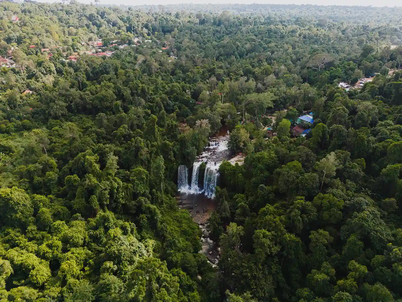 An aerial view of the multi-tiered Phnom Kulen waterfall cascading into a pool amid dense green rainforest featured in a guide on Things to Do in Siem Reap Beyond Angkor Wat.