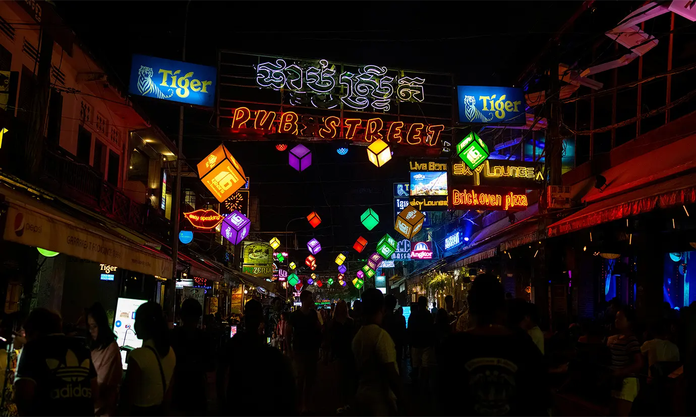 Illuminated Pub Street neon sign and colorful hanging cube lights glowing over crowds of nightlife visitors featured in a guide on Things to Do in Siem Reap Beyond Angkor Wat.