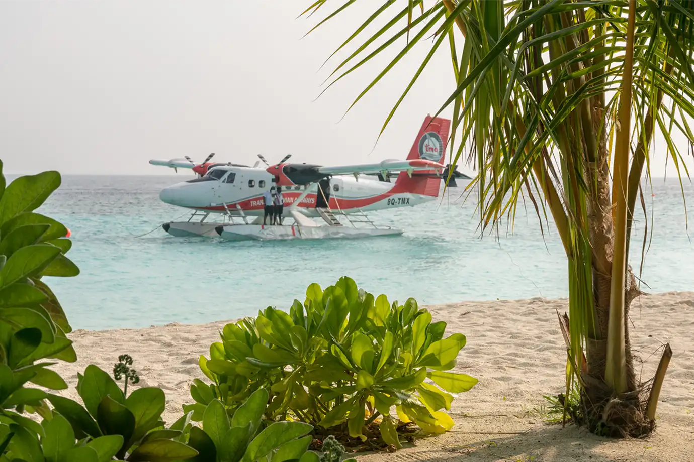 A red and white Trans Maldivian Airways seaplane floating near a tropical sand beach featured in a Maldives Travel Guide for First-Timers.