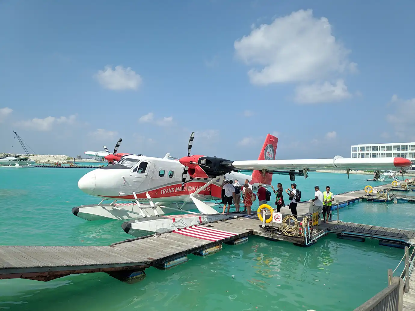 Tourists boarding a red and white seaplane docked at a wooden floating platform over turquoise waters featured in a guide on the Best Time to Visit the Maldives.