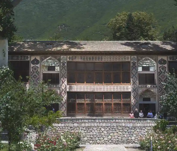 The ornate stained-glass facade and rose garden of the Palace of Sheki Khans set against green forested hills featured in a travel guide on The Ultimate 7-Day Azerbaijan Itinerary.