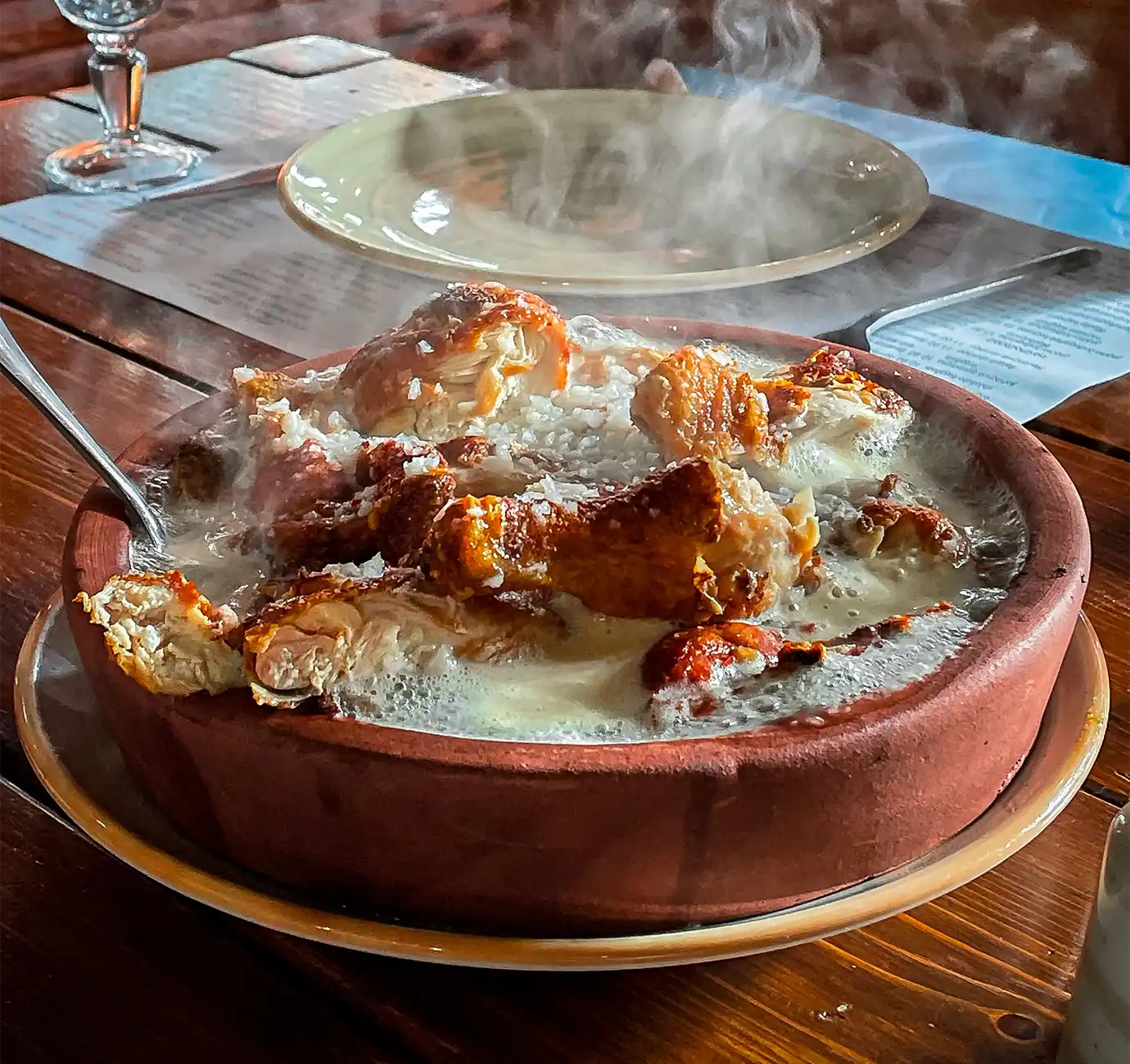 A steaming clay ketsi dish filled with crispy fried chicken bathed in a bubbling garlic cream sauce, illustrating a top dish for a Georgian Food Guide.