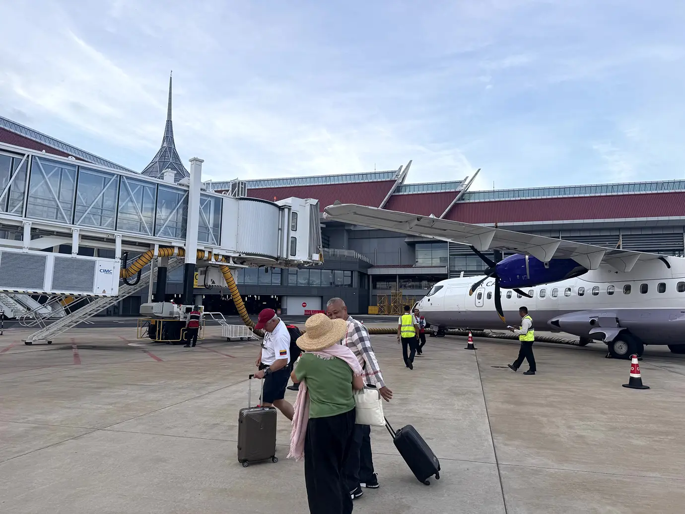 Travelers walking with luggage across the tarmac past a jet bridge and aircraft at Siem Reap Angkor International Airport featured in a travel guide on Cambodia Visa Requirements.
