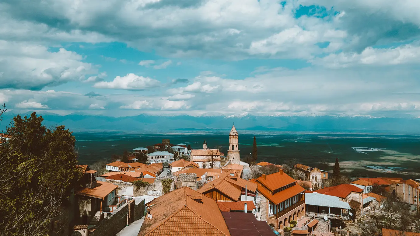 A high-angle view of red-tiled roofs in Sighnaghi overlooking the vast green Alazani Valley and Caucasus mountain range, highlighting historic Places to Visit in Georgia.
