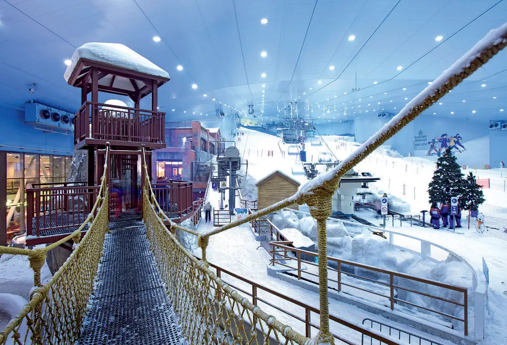 A suspension bridge leading to a wooden lookout tower inside the snowy indoor ski slope complex at Ski Dubai, ideal for visiting Dubai with Kids.