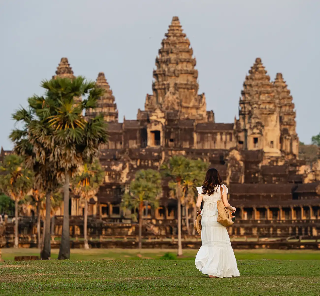 A woman in a white dress walking toward the ancient stone towers of Angkor Wat on a clear day featured in a travel guide on Is Cambodia Safe.