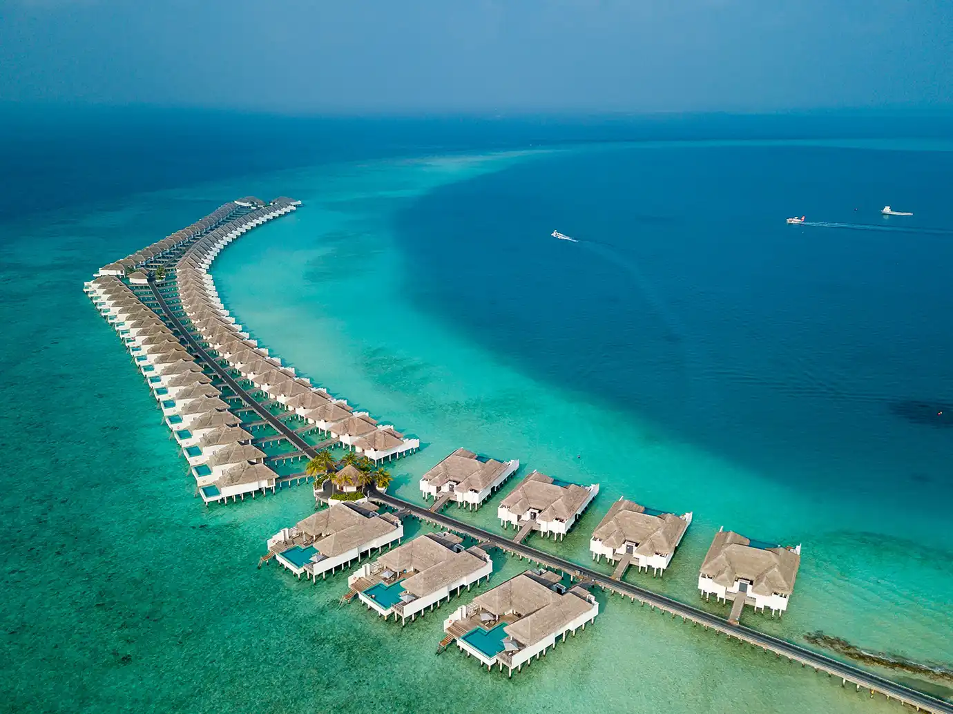 High-angle aerial shot of luxury overwater villas fanning out over turquoise lagoon waters featured in an Oman and Maldives Travel Guide.