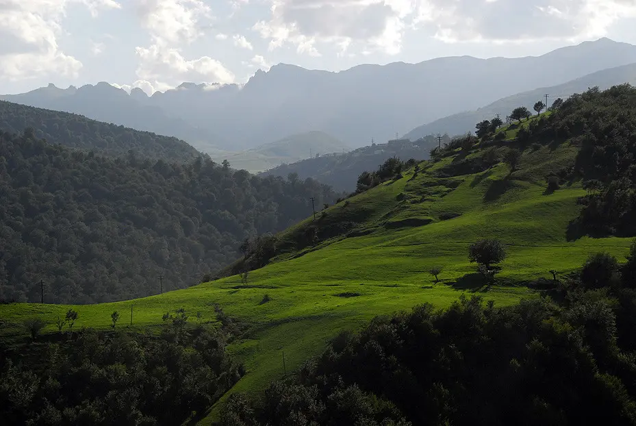 Vibrant green rolling hillsides and dense dark forests framing distant mountain ridges in the Talysh Mountains featured in a travel guide on 5 Must-Visit Destinations in Azerbaijan Beyond Baku.