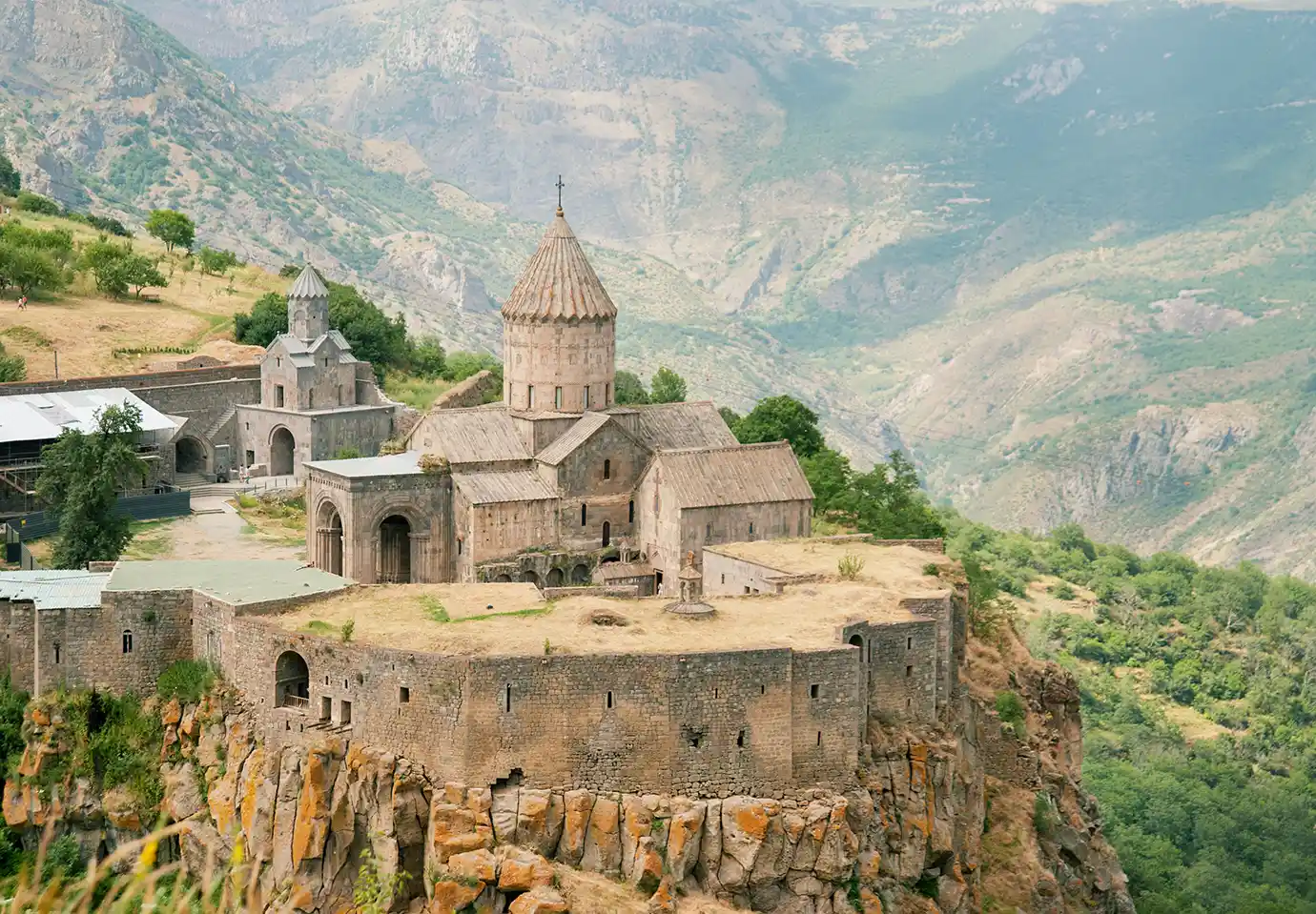 Ancient Tatev Monastery built on a steep cliff edge overlooking a deep mountain canyon featured in a travel guide on 5 Must-See Monasteries in Armenia.