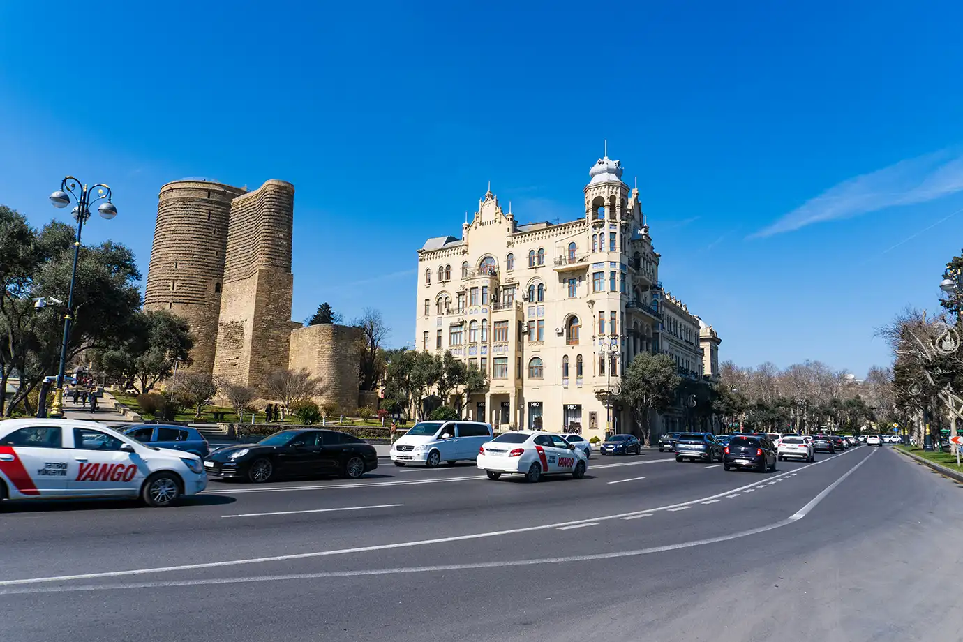 Branded Yango ride-share taxis driving on a paved city street alongside the historical stone Maiden Tower in Baku featured in a travel guide on 10 Essential Things to Know Before Visiting Azerbaijan.