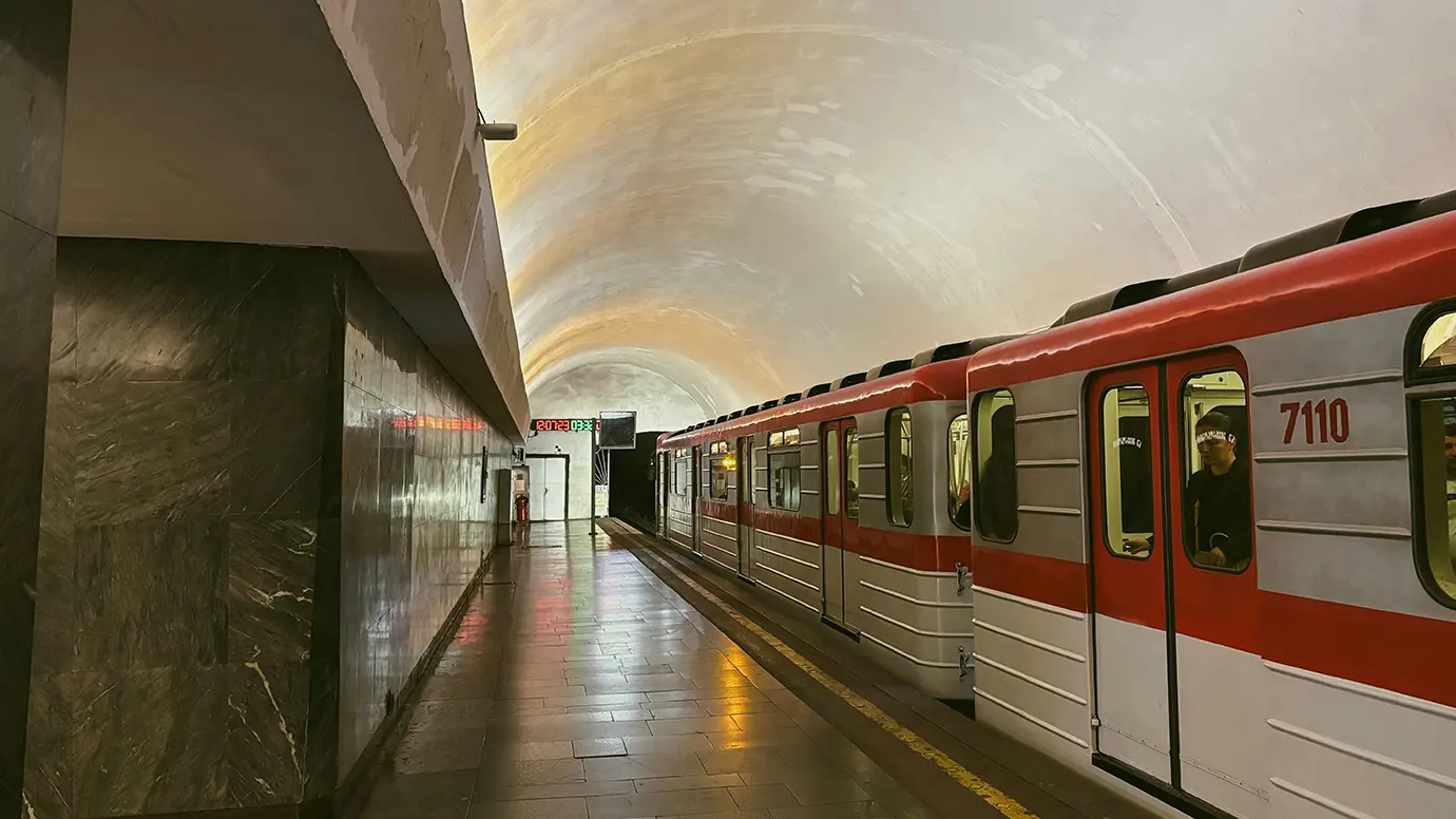 A red and white metro train stopped at an underground subway platform in Tbilisi, highlighting low-cost public transit options for Georgia Travel Cost.