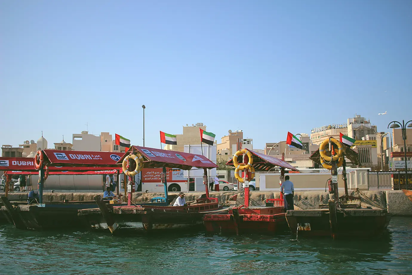 A line of traditional wooden abra boats with UAE flags docked at the stone quay on Dubai Creek, highlighting authentic cultural Things to Do in Dubai.