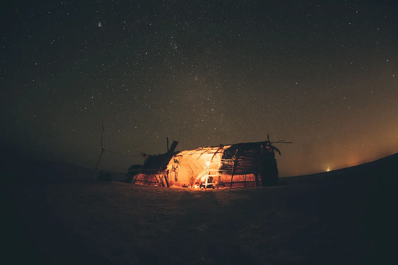 A glowing wooden and thatched desert shelter standing under a clear starry night sky during an overnight Dubai Desert Safari.