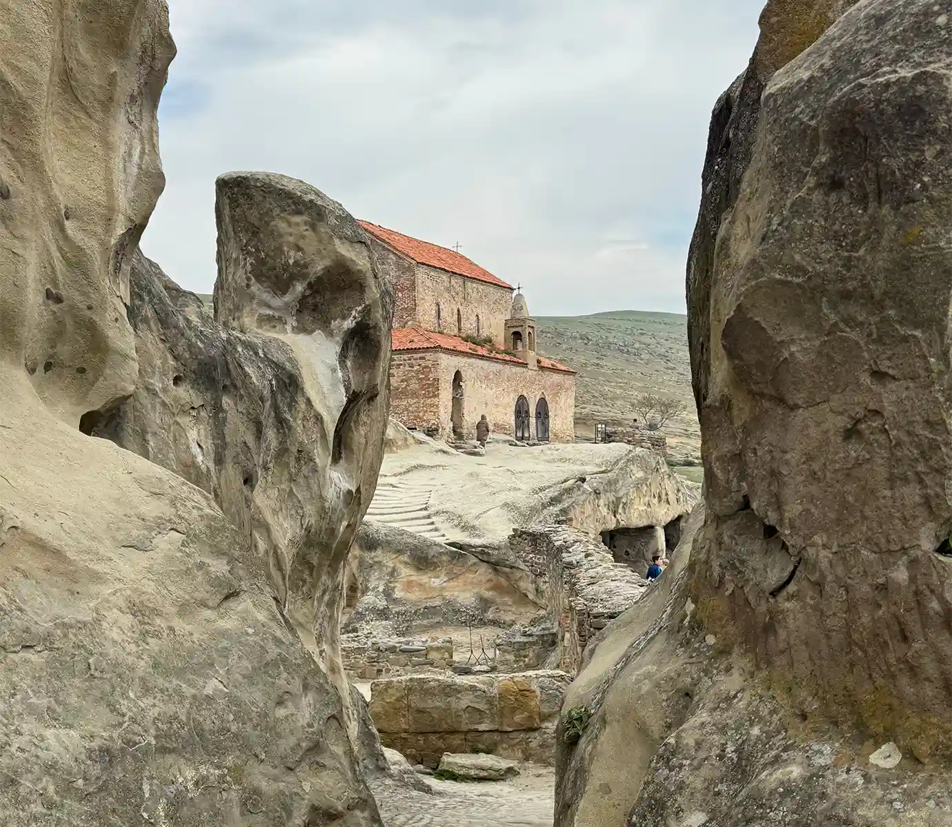 A orange-tiled brick church framed by carved rock formations inside the ancient Uplistsikhe cave city, illustrating archaeological Places to Visit in Georgia.