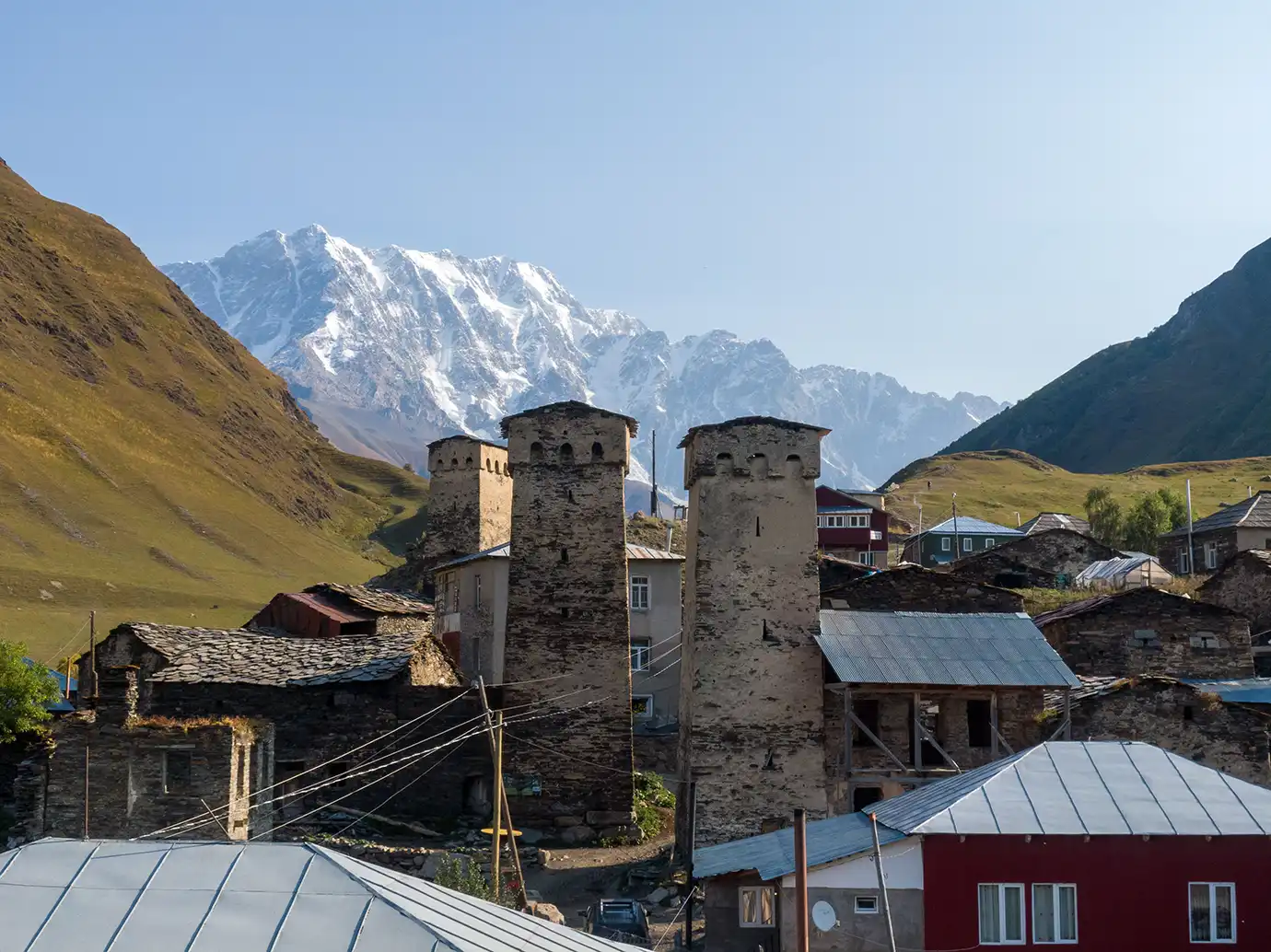 A panoramic view of ancient Svan stone tower houses in the village of Ushguli set against towering snow-capped mountain peaks, highlighting top Places to Visit in Georgia.