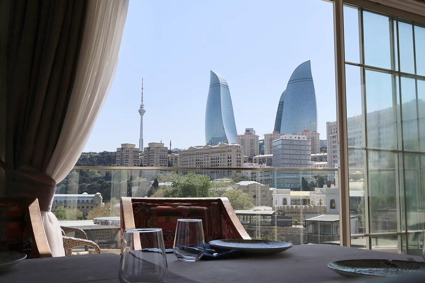 A high-end dining table set with glassware framing a scenic outdoor view of the Flame Towers and Baku skyline featured in a travel guide on How Much Does a Trip to Azerbaijan Cost?