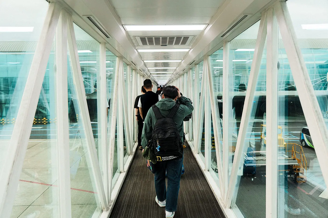 Travelers carrying backpacks walking through a glass jet bridge towards the airport terminal, illustrating smooth entry under updated Dubai Visa Requirements.