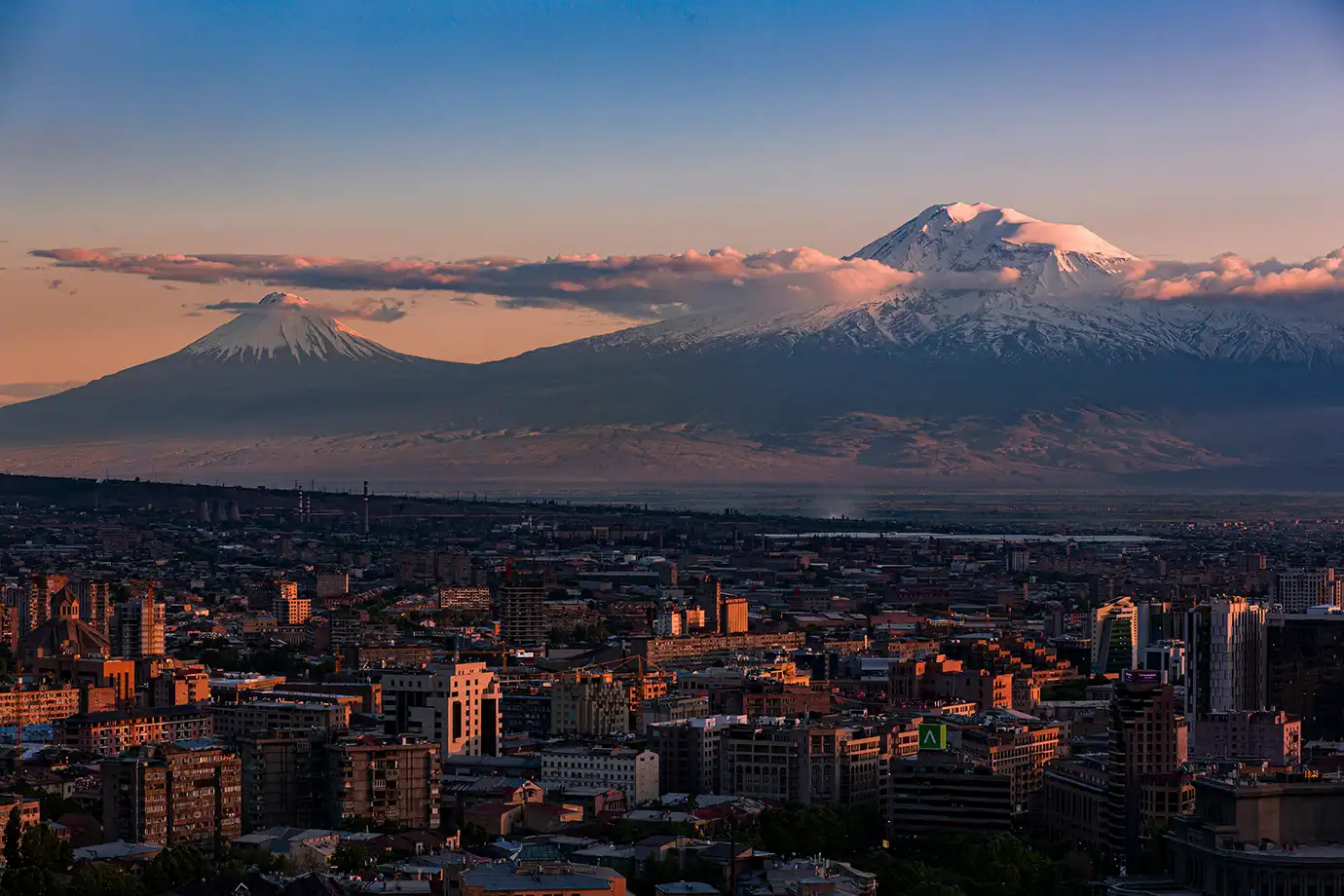 A sunset view over the cityscape of Yerevan with snow-capped Mount Ararat towering on the horizon featured in a travel guide on The Ultimate 7-Day Armenia Itinerary.