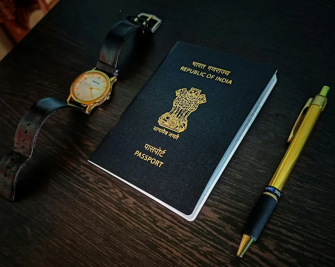 An official Indian passport resting on a dark wooden tabletop beside a gold pen and watch, illustrating document preparation for Hong Kong Visa Requirements.
