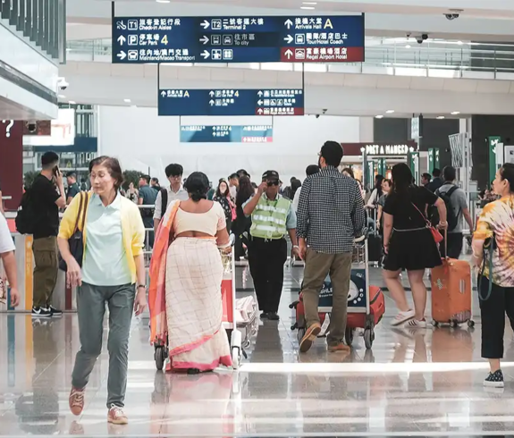 International travelers walking through a spacious airport arrivals hall with overhead directional signage, illustrating entry procedures for Hong Kong Visa Requirements.