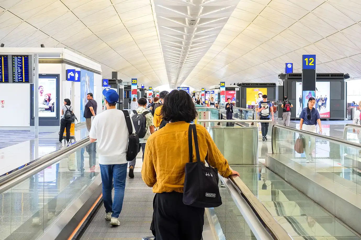 Passengers riding a moving walkway through a bright, modern airport concourse toward immigration, representing arrival procedures for Hong Kong Visa Requirements.