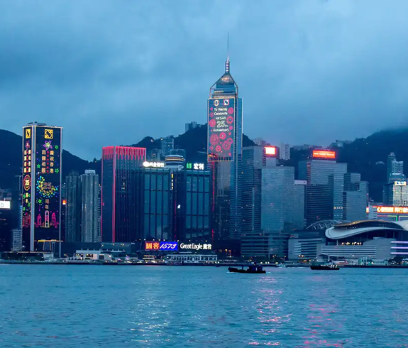 A panoramic dusk photograph of Victoria Harbour illuminated by vibrant city lights against high-rise commercial buildings, highlighting top scenic highlights for Things to Do in Hong Kong.